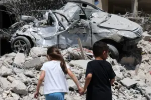 En la foto, niños caminando frente a vehículos dañados y escombros tras un ataque israelí, en Maaroub (Líbano)
