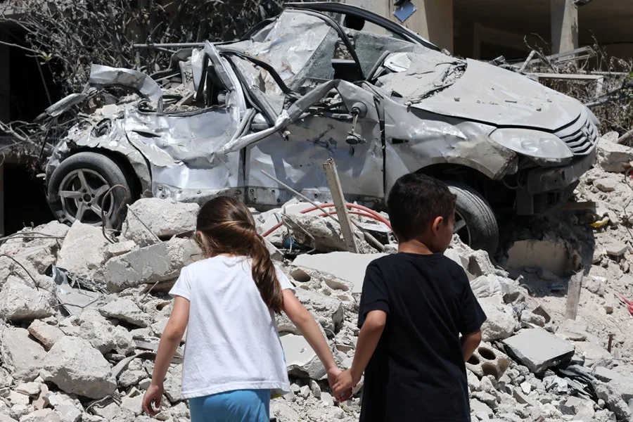 En la foto, niños caminando frente a vehículos dañados y escombros tras un ataque israelí, en Maaroub (Líbano)