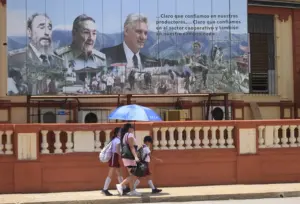 En la foto, personas caminando frente a una valla que muestra las imágenes del presidente de Cuba, Miguel Diaz-Canel (d), y de los expresidentes Raúl (c), y Fidel Castro, en La Habana