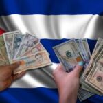 En la foto, dos manos ante una bandera cubana, con pesos y dólares
