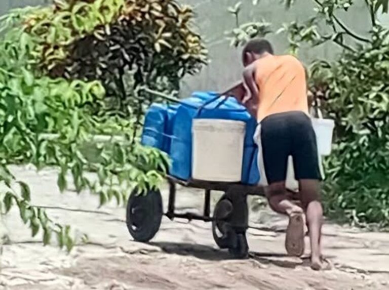 En la foto, un niño cubano empuja una carretilla cargada con bidones de agua
