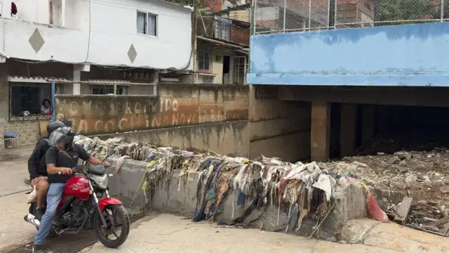 Al menos seis desaparecidos y decenas de viviendas afectadas en Venezuela por las lluvias 1 En la foto, Personas transitan frente a un canal de desagüe con basura tras las fuertes lluvias este domingo, en Caracas
