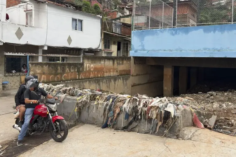 En la foto, Personas transitan frente a un canal de desagüe con basura tras las fuertes lluvias este domingo, en Caracas