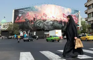 En la foto, Una mujer iraní con velo pasa junto a un cartel antiestadounidense en la plaza Enghelab, en el centro de Teherán