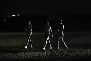 En la foto, la luz de un vehículo ilumina a jóvenes que caminan a oscuras por el malecón de La Habana