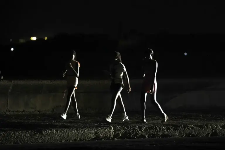 En la foto, la luz de un vehículo ilumina a jóvenes que caminan a oscuras por el malecón de La Habana