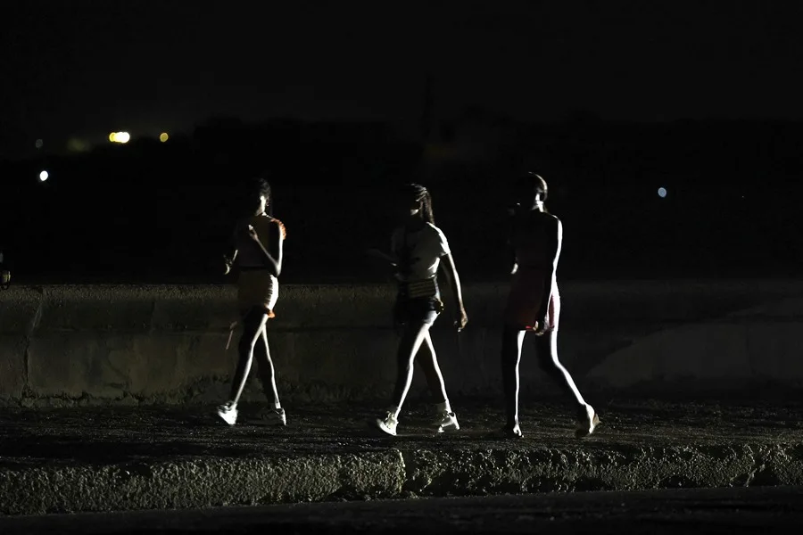 En la foto, la luz de un vehículo ilumina a jóvenes que caminan a oscuras por el malecón de La Habana