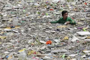 En la foto, Un trabajador en labores de limpieza para recoger basura y escombros flotantes acumulados en un canal en Filipinas