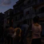 Personas hacen cola al anochecer frente a edificios deteriorados durante un apagón en Cuba