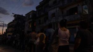 Personas hacen cola al anochecer frente a edificios deteriorados durante un apagón en Cuba