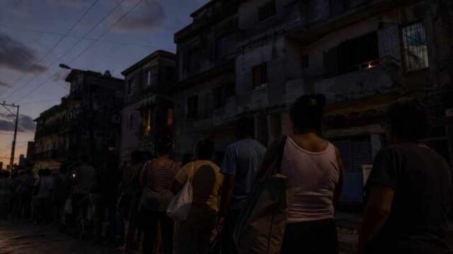 Personas hacen cola al anochecer frente a edificios deteriorados durante un apagón en Cuba