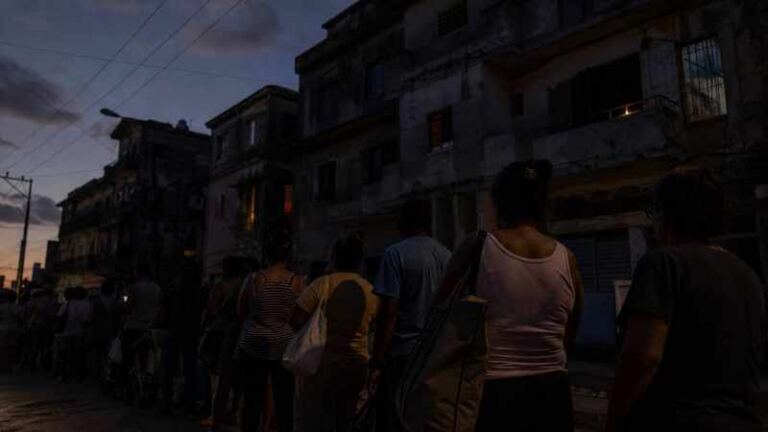 Personas hacen cola al anochecer frente a edificios deteriorados durante un apagón en Cuba