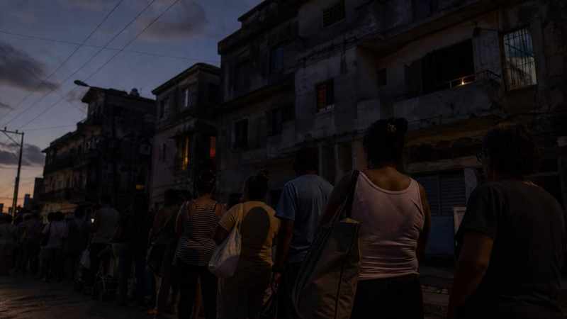 Personas hacen cola al anochecer frente a edificios deteriorados durante un apagón en Cuba