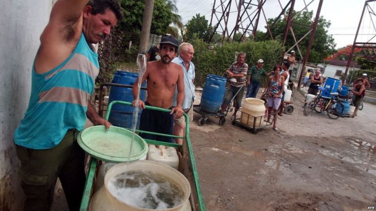 En la foto, cubanos buscan agua en lo que tengan a mano