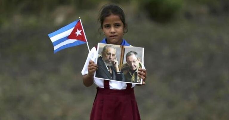 En la foto, una niña cubana con uniforme escolar, una bandera y fotos de Raúl y Fidel Castro