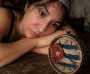 En la foto, una mujer recostada ante un reloj con la bandera cubana en su esfera