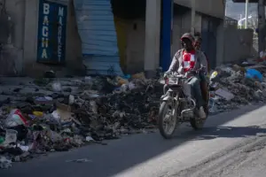 En la foto, personas movilizándose en una motocicleta por una calle cubierta de basura, en Puerto Príncipe (Haití)