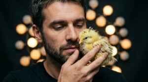 En la foto, un hombre joven acaricia un pollito enfermo
