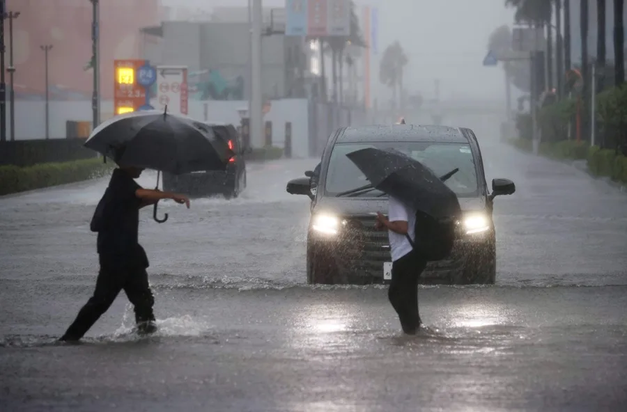 En la foto, Dos personas tratan de cruzar una calle inundada en Funabashi, prefectura de Chiba, cerca de Tokio