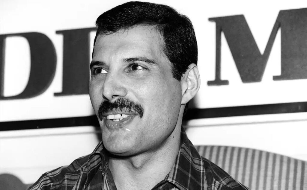 Freddie Mercury: biografía de la voz y el alma de Queen 2 Retrato en blanco y negro de Freddie Mercury con bigote y camisa de cuadros.