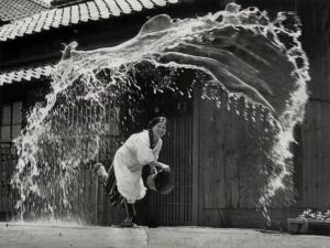 En la foto, una mujer japonés lanza agua a la calle