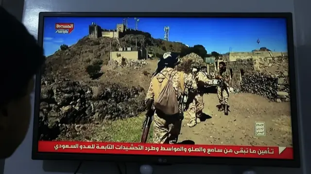 En la foto, Una persona observa una transmisión televisiva que muestra a combatientes hutíes en Saná (Yemen)