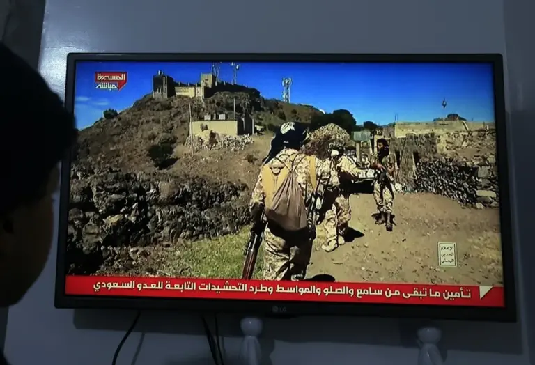 En la foto, Una persona observa una transmisión televisiva que muestra a combatientes hutíes en Saná (Yemen)